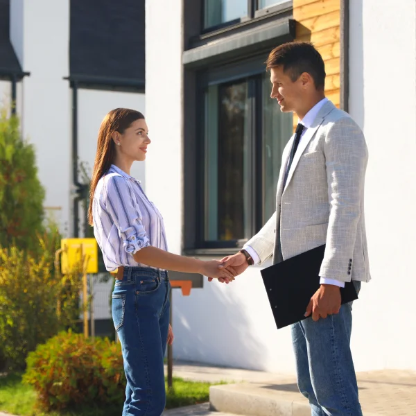 Un homme et une femme se serrent la main devant une maison, symbolisant une transaction immobilière de luxe.