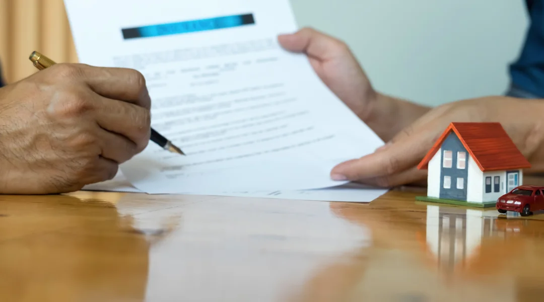 Un homme signe un contrat avec un modèle de maison, illustrant une transaction de courtage immobilier.
